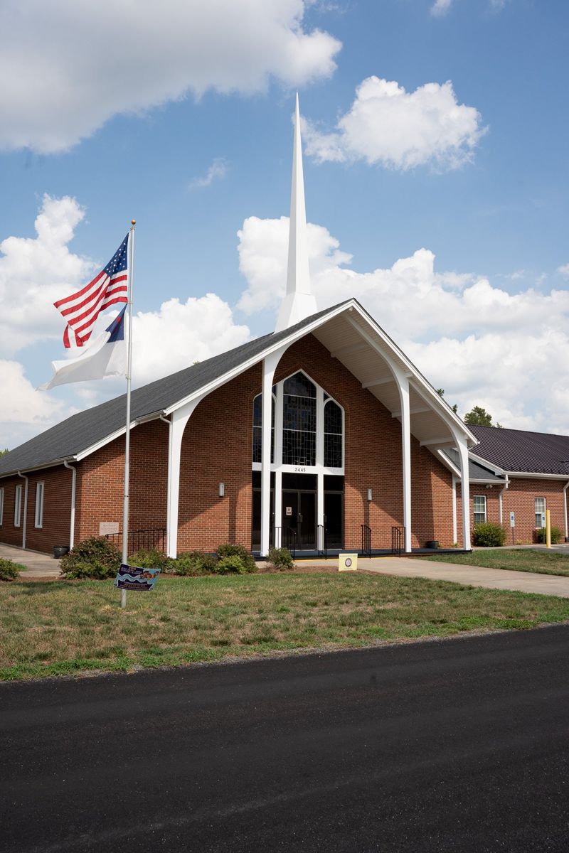 The red brick front of Altamahaw Baptist Church with its white steeple and arched entrance under a blue sky